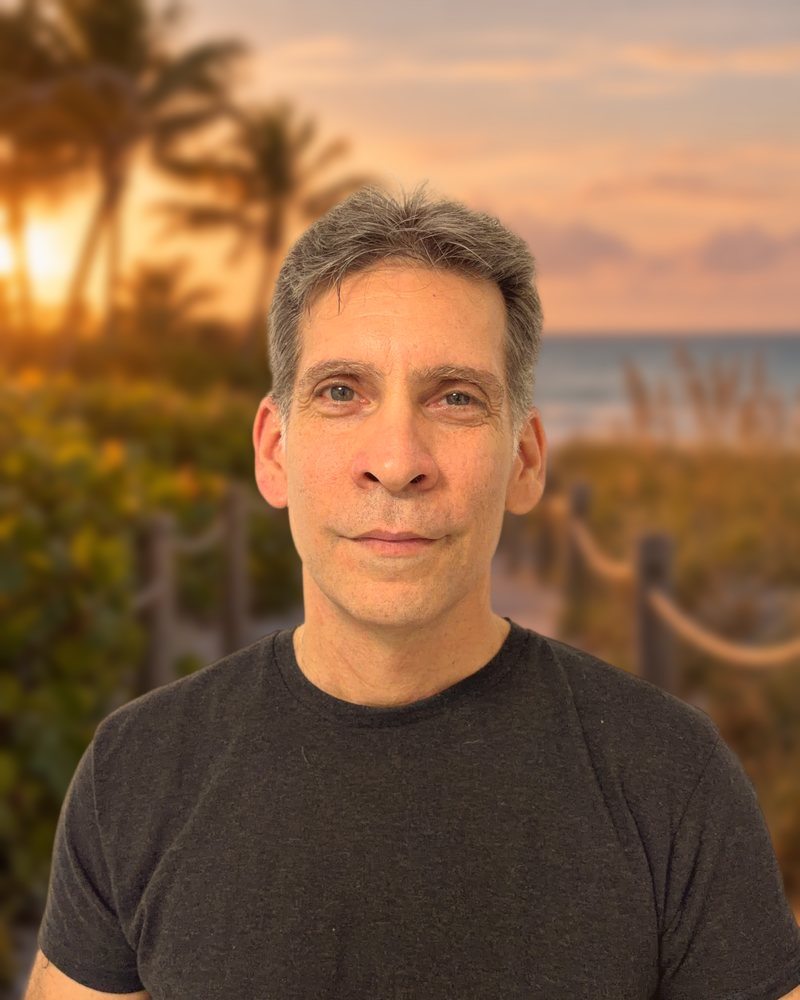 Israel Maya, author, smiling on a Miami boardwalk at sunset